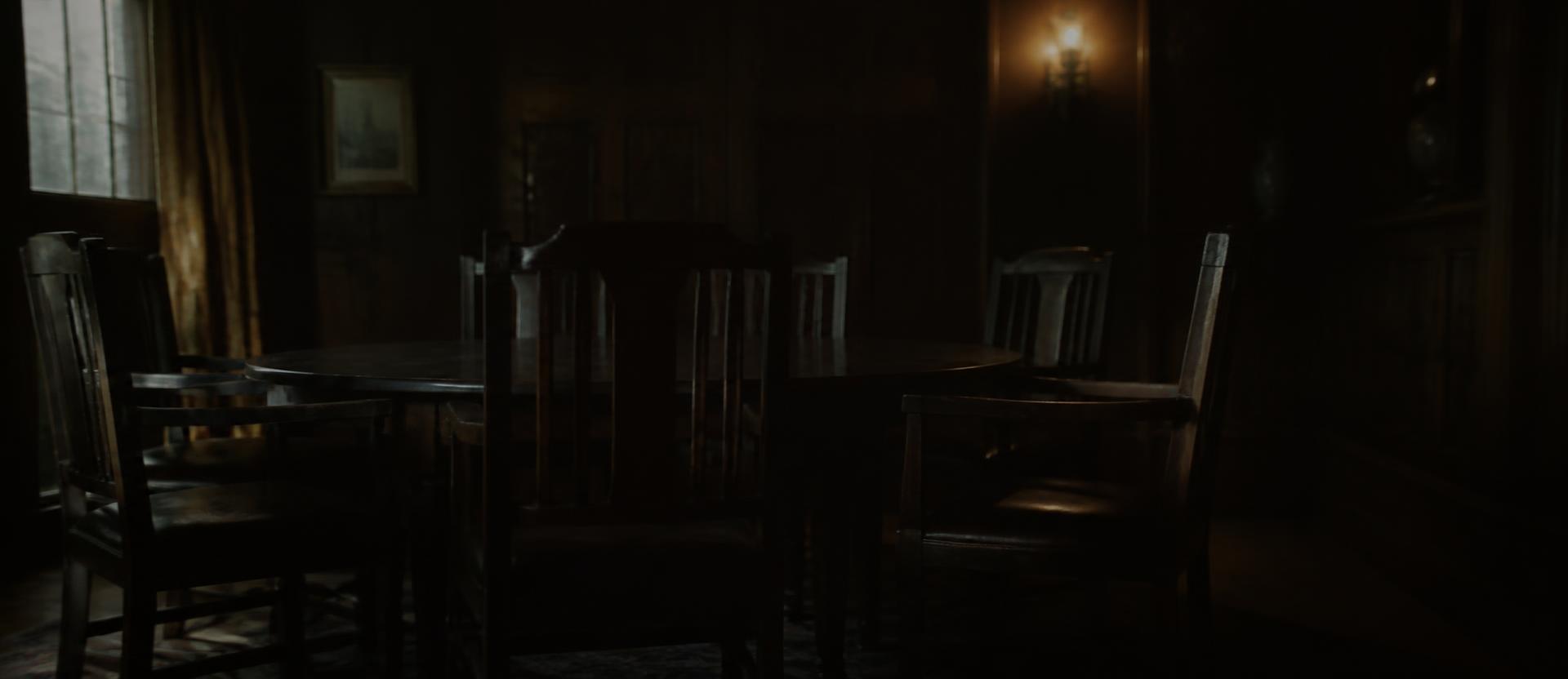 A dim room with chairs around a table, shot wide